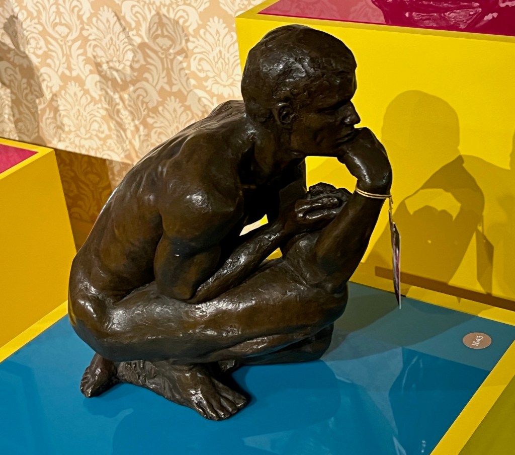 A small bronze statue of a man crouching down low, with one hand on his chin while he's deep in thought.