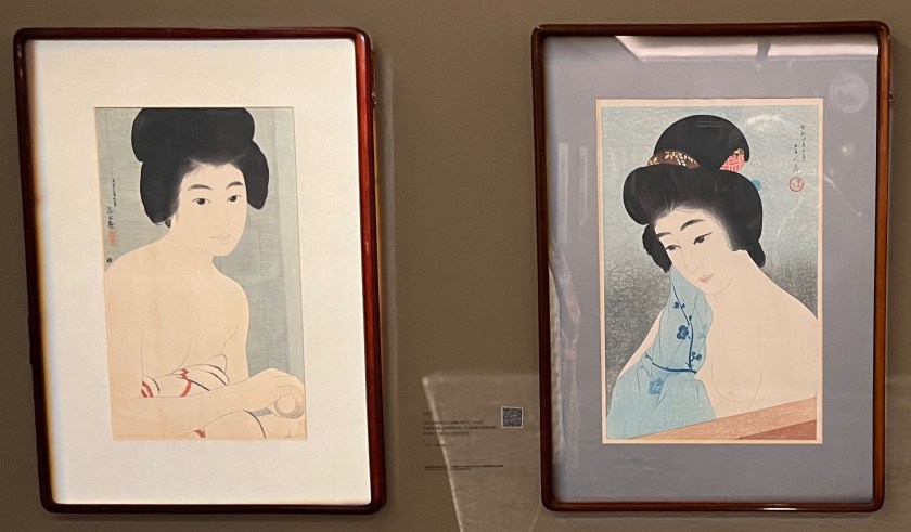 2 woodblock prints of Japanese women. On the left, a young woman is about to apply oshiroi, a powder foundation associated with geisha and their apprentices. She sits before an unfurled bamboo blind, her gaze reserved and vague. The woman on the right, meanwhile, has a light blue cloth with a dark blue pattern of flowers on a stem draped over her right shoulder, covering her right breast, while her left breast remains exposed.
