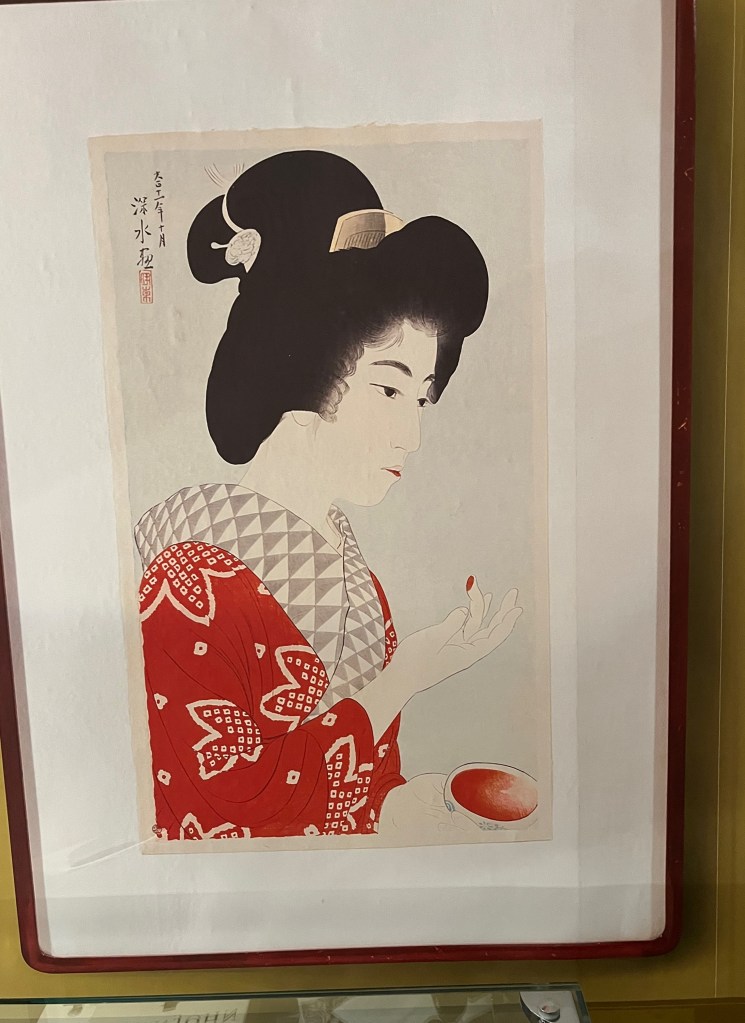 Woodblock print painting of a young Japanese woman wearing a red kimono patterned in white with stylised maple leaves.