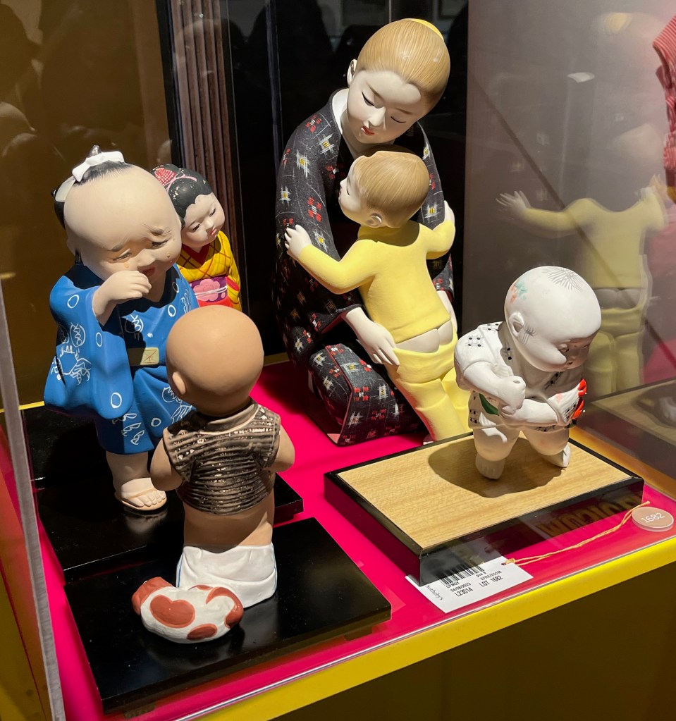 Four clay figures of Japanese children. One of them is being hugged by their mother, but its trousers are pulled down slightly, revealing its buttocks.