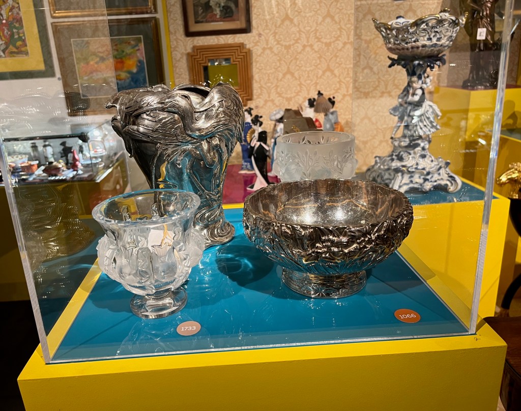 A glass case showing 2 metal and 2 glass vases of different sizes with ornate designs.