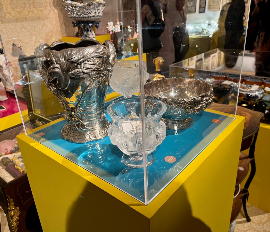 Corner view of a glass case showing 2 metal and 2 glass vases of different sizes with ornate designs.