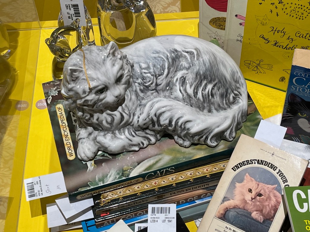 A porcelain model of a grey cat with lots of ruffled fur laying down.