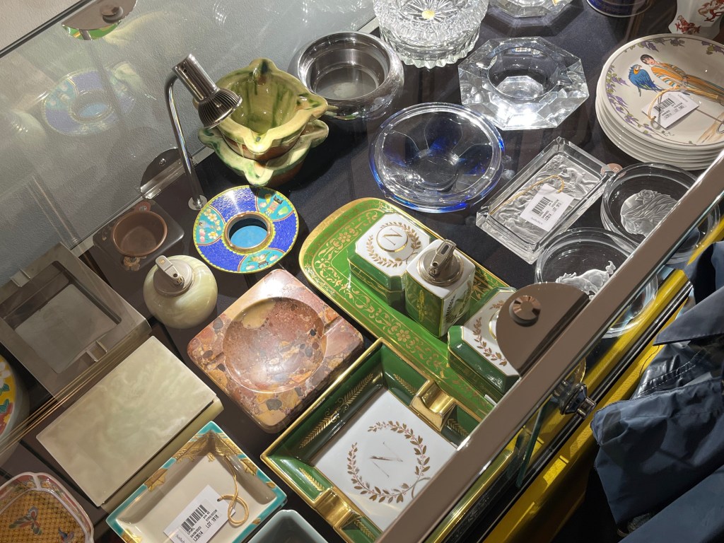 Part of a large collection of ashtrays with varied designs, along with a few cigarette boxes and lighters, in the Freddie Mercury exhibition.