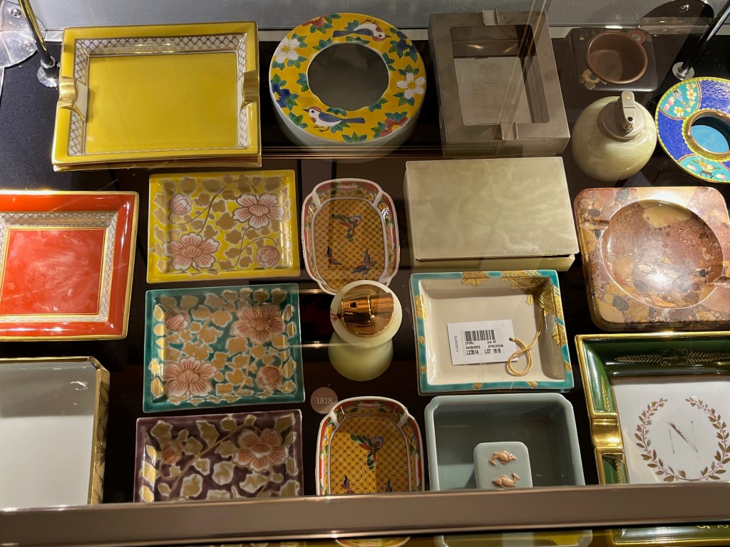 A large collection of ashtrays with varied designs, along with a few cigarette boxes and lighters, in the Freddie Mercury exhibition.