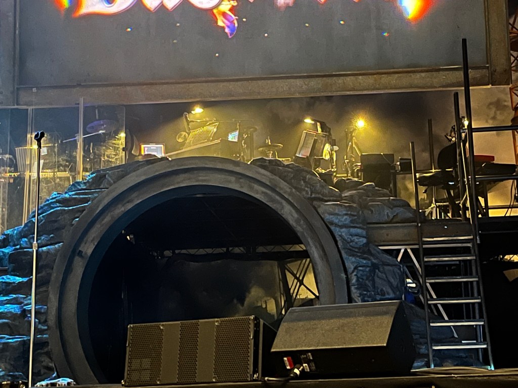 Part of the stage for the Bat Out Of Hell musical, showing the opening to a large tunnel, above which is a platform for the musicians, reached by a small flight of steps to the right of the tunnel.