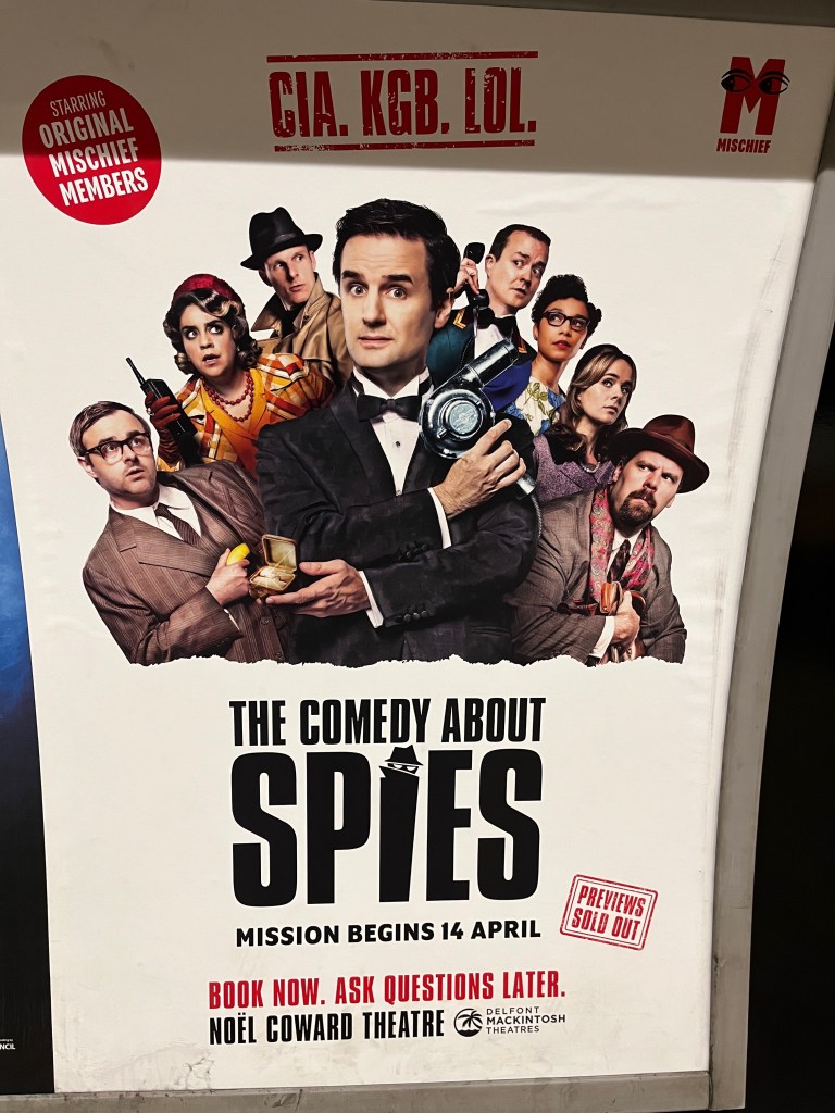 Poster for The Comedy About Spies. The top half of the poster features an image of the various characters. In the centre is a smartly dressed man in a black jacket, white shirt and black bow tie. His right arm is across his chest, holding up a hairdryer as if posing with a gun, James Bond style. His left hand crosses his chest below that, holding an open ring box with a glittering ring inside. The other 7 characters are fanned out around him in the background, looking over at him. At the very top of the poster is the tagline CIA, KGB, LOL, while a red circle to the left has white text saying starring original Mischief members. In the bottom half of the poster, below the show's title, text says mission begins 14 April, book now, ask questions later.