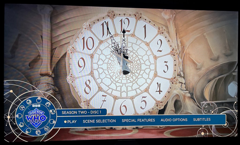 Main menu for the Blu-ray of Doctor Who Season 2, showing a large clock face, with the time showing as 5 minutes to midnight. Across the bottom are options for  Play, Scene Selection, Special Features, Audio and Subtitles.