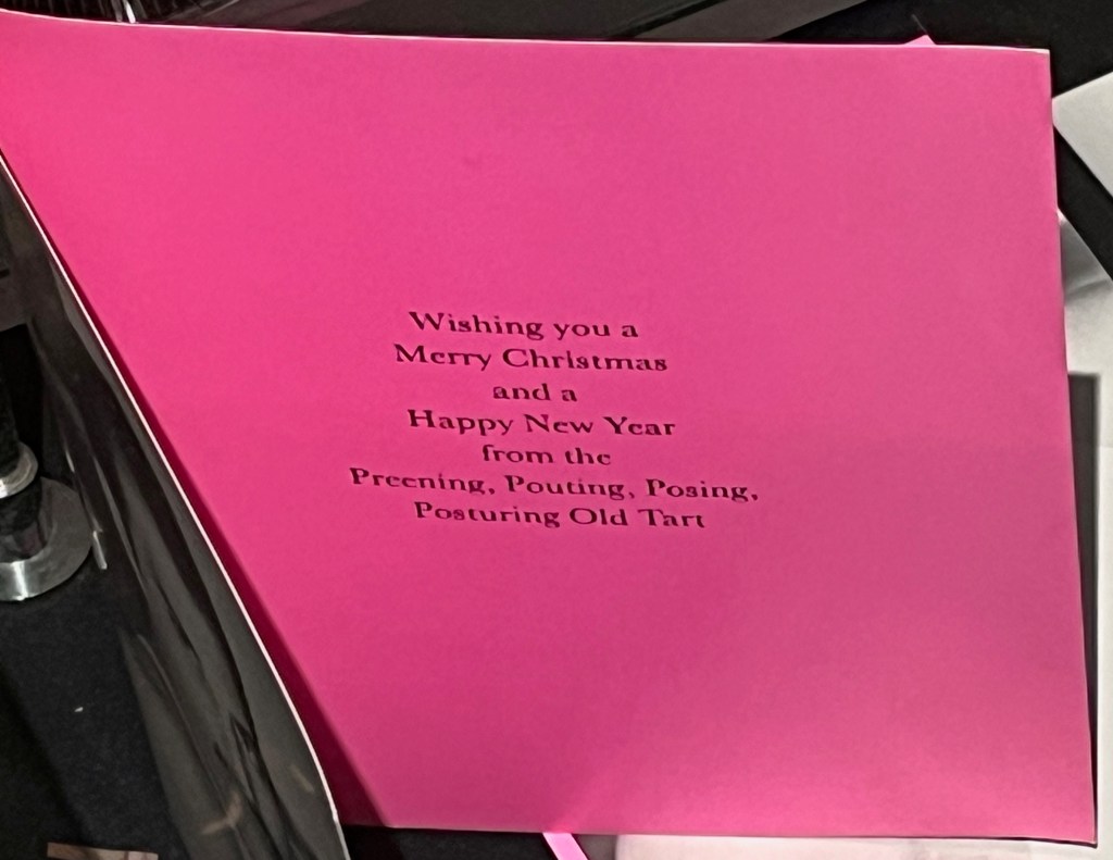 A vibrant pink-coloured card from Freddie Mercury, with black text that says Wishing you a Merry Christmas and a Happy New Year from the Preening, Pouting, Posing, Posturing Old Tart.