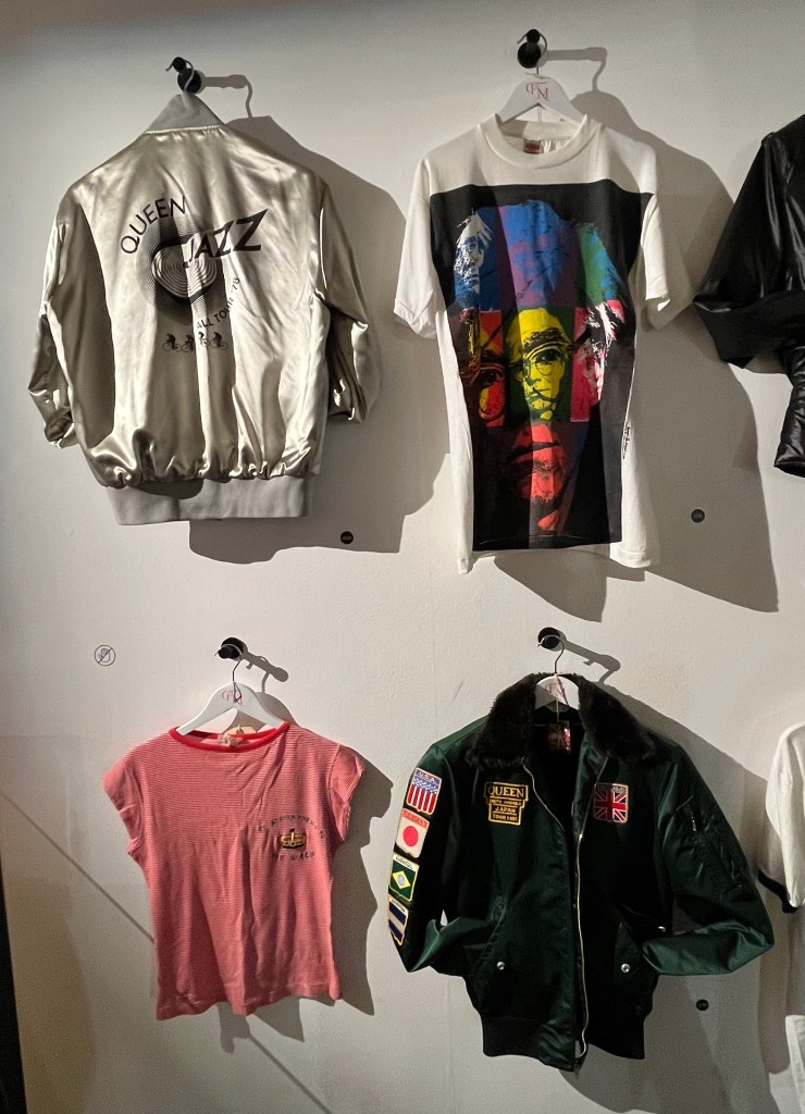 Metallic silver satin bomber jacket for Queen's Jazz Tour 1978, a green satin bomber jacket with brown imitation fur collar for Queen's South America and Japan Tour 1981,
a white T-shirt screen-printed with multi-coloured images of Andy Warhol’s self-portrait making up a single head portrait of Warhol, and a red and white stripe cap-sleeved T-shirt with crown motif embroidered in gold, green and black thread to front, and in green the text ‘By Appointment To The Queen’.