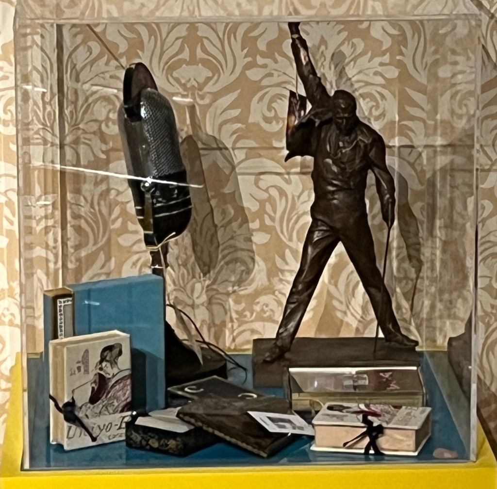A novelty radio in the shape of a large old-style radio microphone, and a bronze statuette of Freddie Mercury in his trademark pose, standing with legs apart and looking own, his right arm raised high in the air triumphantly.