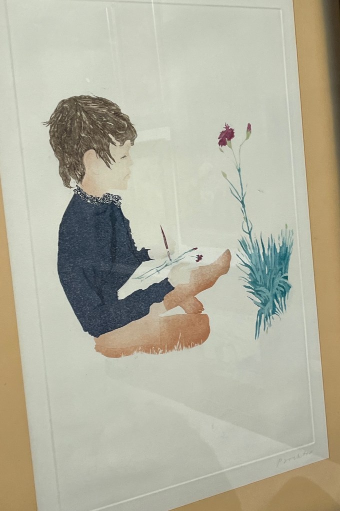 A painting of a young boy in a blue jumper sitting cross-legged on the ground with a pad on his lap, as he paints a carnation that's in front of him.