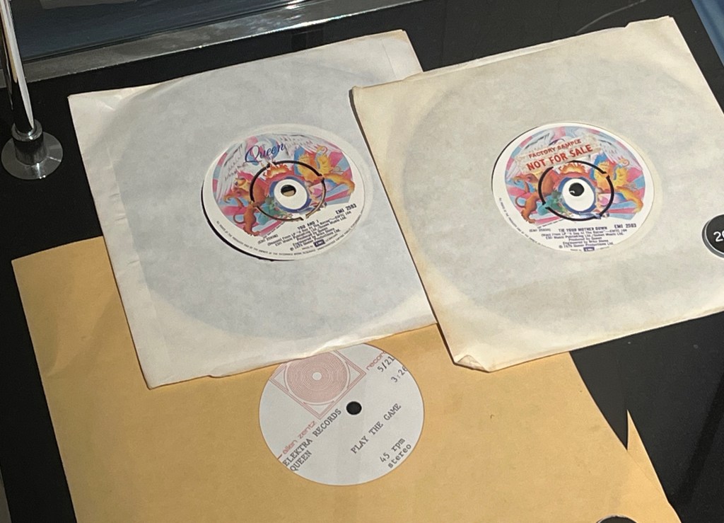 7-inch vinyl discs for the Queen songs You And I, Tie Your Mother Down and Play The Game. The discs for the first 2 songs include the colourful design of the band's crest from the album A Day At The Races.