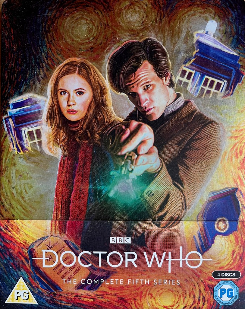 Front cover for the Doctor Who Series 5 Blu-ray steelbook. It shows Matt Smith as the Doctor, with a stern expression on his face as he points his sonic screwdriver straight at us. His companion Amy Pond, with red hair and a red scarf over her dark clothing, stands next to him, also looking towards us. In the background, the Tardis has split in two amongst a swirling explosion.