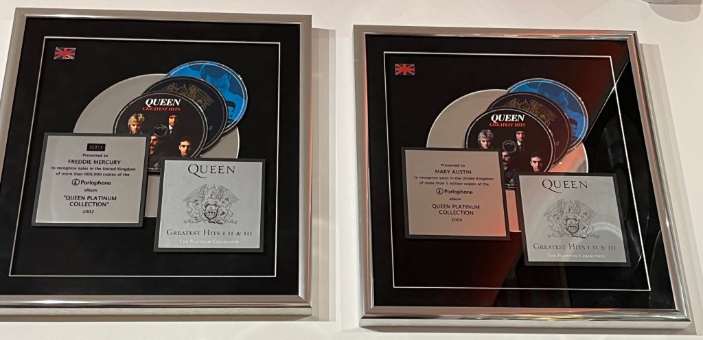 Two sales awards for Queen's Platinum Collection – Greatest Hits 1, 2 and 3. Each award is a large box with a black background. A large platinum disc sits in the centre of the background, overlaid with the 3 Greatest Hits discs, which overlap each other. To the left is a silver plaque explaining why the award has been given, and to the lower right is an image of the outer cover of Greatest Hits 1-3 box set, showing the band's crest on a silver background.