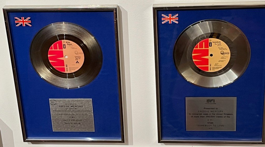 Large silver disc awards in display boxes with blue backgrounds, for the Queen singles Killer Queen and Somebody To Love.