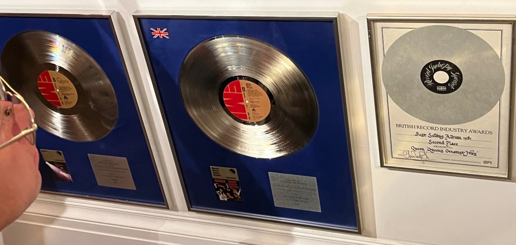 Large silver disc awards in display boxes with blue backgrounds, for the Queen albums Queen and Sheer Heart attack, along with a certificate for Greatest Hits, awarding it Best Selling Album 1981, Second Place.