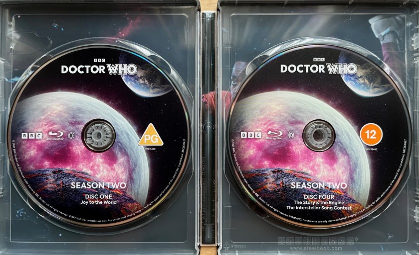 Blu-ray discs in the steelbook for Doctor Who Season 2. They all carry the same artwork, showing a planet or moon covered in red patches as if it's being destroyed, while a burning meteor flies towards it from our direction. Planet Earth is in the top right.
