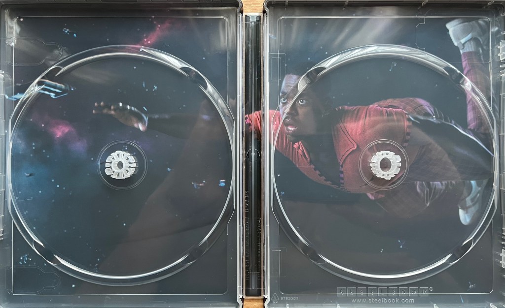 The interior of the Blu-ray steelbook for Doctor Who Season 2, when the discs have been removed. Behind the panels holding the discs is an image of Ncuti Gatwa as the Doctor reaching out as he floats through space with a look of alarm on his face.
