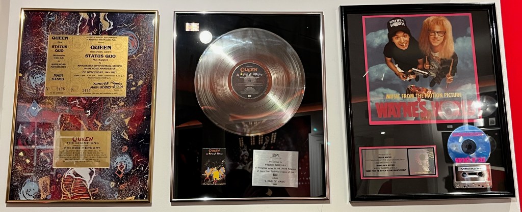 Commemorative gold ticket for Queen and Status Quo at Manchester City Football Ground on 16 July 1986, and disc awards for the albums A Kind Of Magic and the Wayne's World soundtrack.
