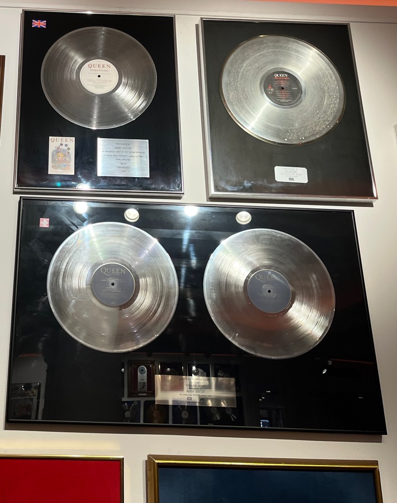 Disc sales awards for Innuendo and Greatest Hits 1 and 2. The Greatest Hits 2 award has 2 large discs inside its wide case, while the other two awards have just one disc each.