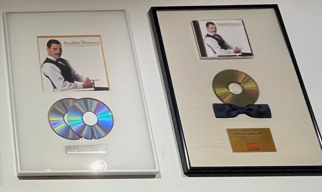 2 disc sales awards for The Freddie Mercury Album. They both show the album cover, with one having 2 overlapping CDs beneath it, while the other has a CD adorned with a blue satin bow tie at the bottom of it.