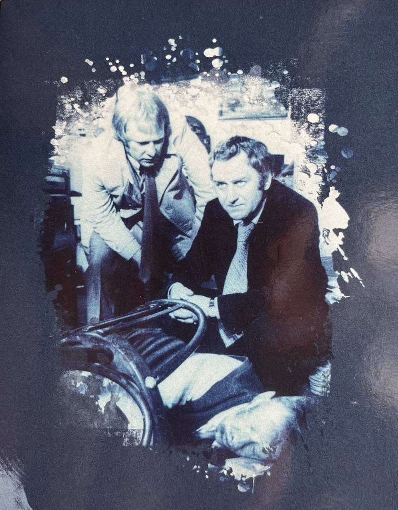 A blue-tinted image from one of the panels in the Blu-ray box set for The Sweeney Series 1, showing Regan and Carter squatting over a beaten-up male body lying on the ground.