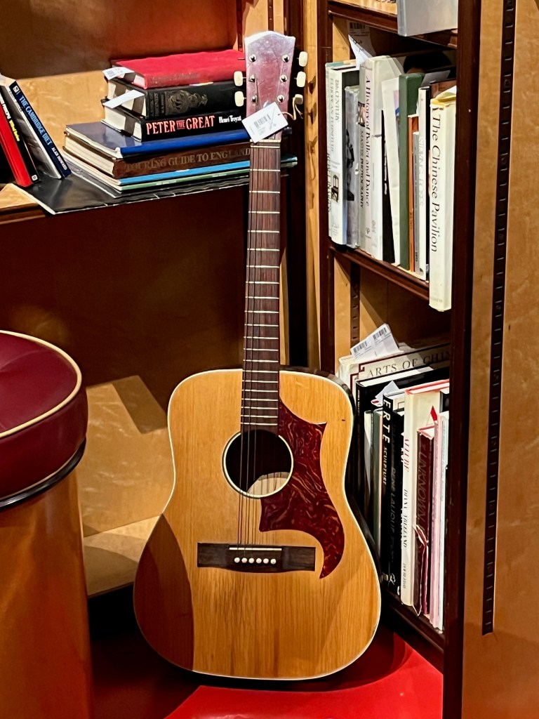 An acoustic guitar, with the head in a natural wood colour, but with a large, curved black shape around one side of the sound hole in the centre.