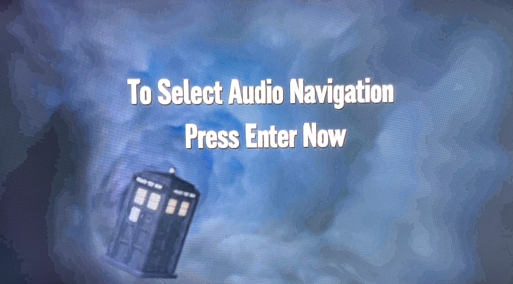 A screen from the audio navigation menu on the Doctor Who Series 6 Blu-ray. Against a static background of the swirling blue time vortex, with the Tardis in the bottom left, there is large, bold, white text in the centre of the screen that says to select audio navigation press Enter now.