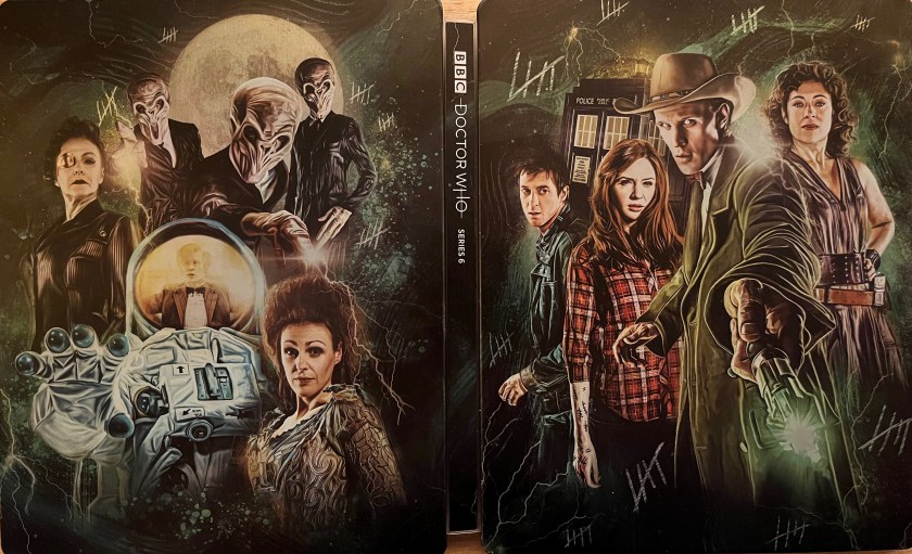 The cover spread artwork for the Doctor Who Series 6 Blu-ray steelbook. The front cover, on the right, shows Matt Smith's Doctor standing in a long brown jacket and a cowboy hat, as he points his sonic screwdriver in front of him, towards us. To his left, companions Amy and Rory are standing together, with the Tardis behind them, while River Song is standing to the right of the Doctor. The back cover on the left, meanwhile, shows a white astronaut's suit, and reflected in the helmet's window is an image of the Doctor regenerating. Around the astronaut are some of the other characters from the series, including Madame Kovarian, The Silence and the female embodiment of the Tardis. Across the background of the entire steelbook cover is a stone wall on which are tally marks in groups of 5 lines, as if someone has been marking time while imprisoned.