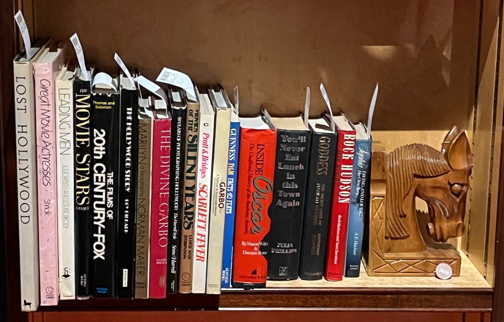 A collection of 17 books about Hollywood and film stars, including titles about Marilyn Monroe, Greta Garbo and Rock Hudson. Next to them is a wooden bookend carved in the shape of a horse's head.