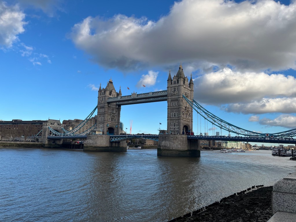 Tower Bridge, with a couple of large grey and white clouds above and behind it in the blue sky.