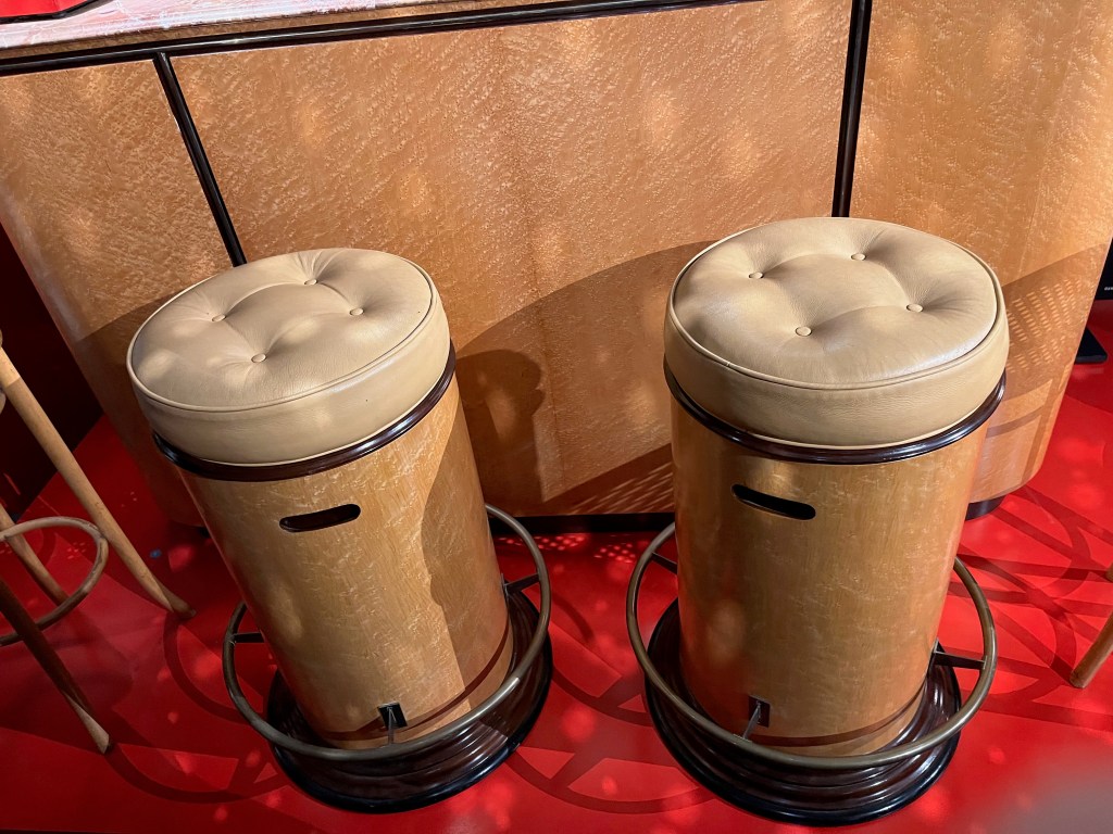 Two round mahogany-panelled bar stools, with a cushioned seat on top and a metal ring around the bottom for resting feet on.