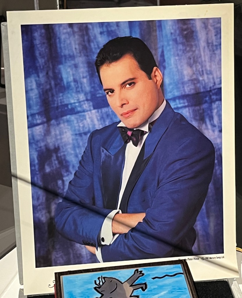 Photo of Freddie Mercury dressed smartly in a dark blue suit over a white shirt with a black bow tie.