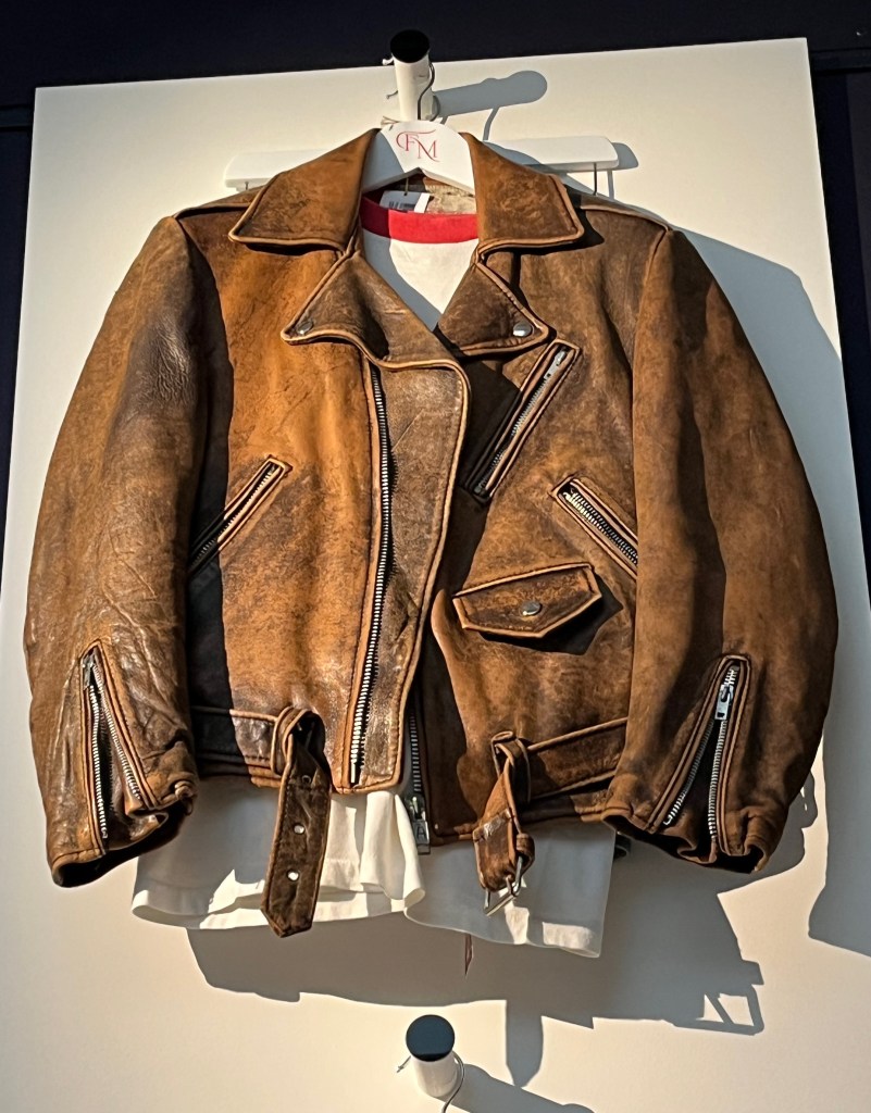 A biker-style jacket of distressed brown leather with large zip fastenings to front, diagonal pockets and cuffs, one flap pocket with press-stud fastening to left side, and integral belt at hips, fastening with a white metal buckle.