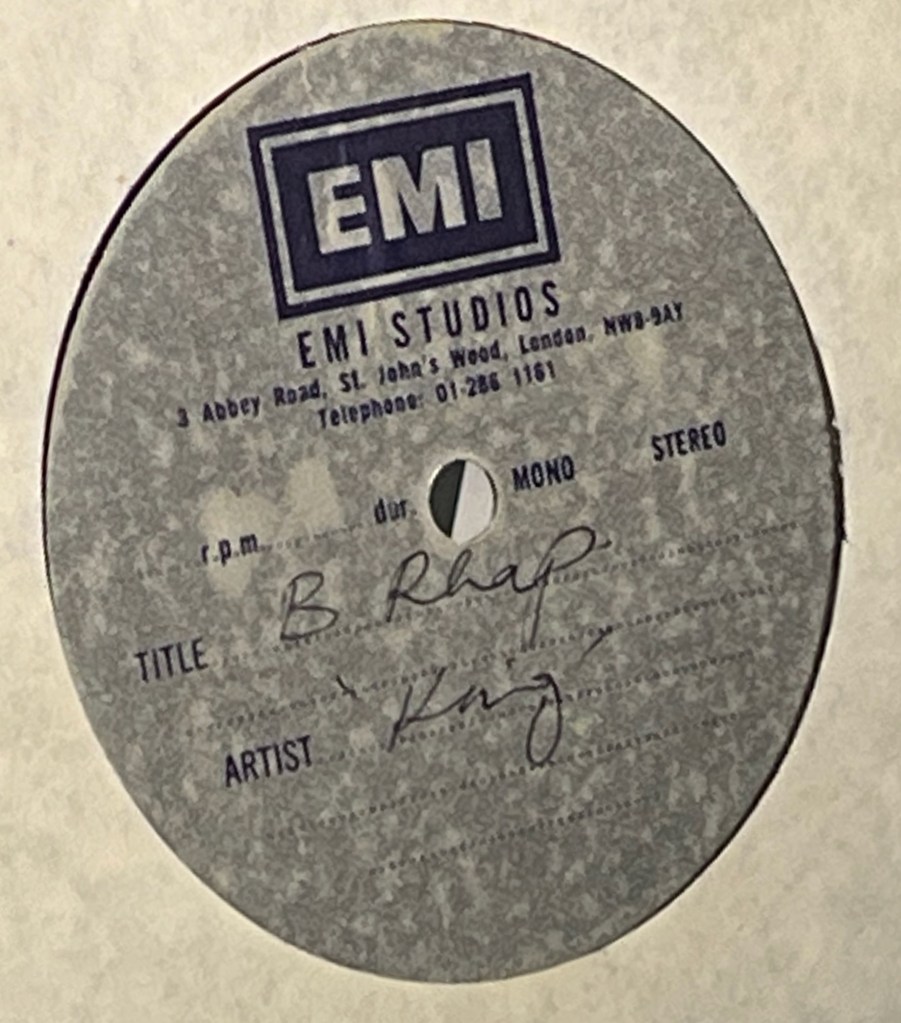 A 7-inch acetate record for Bohemian Rhapsody by Queen. Below the EMI logo and address, handwriting over the grey background of the disc labels the song as B. Rhap and the artist as King rather than Queen.