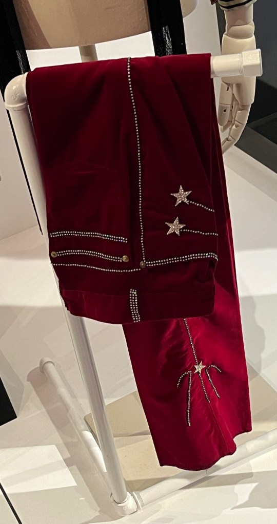 Burgundy velvet trousers, embellished with diamanté in an elaborate shooting-star pattern, the front and back pocket edges and belt loops embroidered with double and triple rows of diamanté.