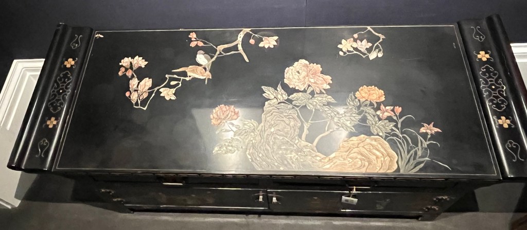 The top of a black lacquer cabinet with a colourful design of flowers and greenery covering some of the surface.