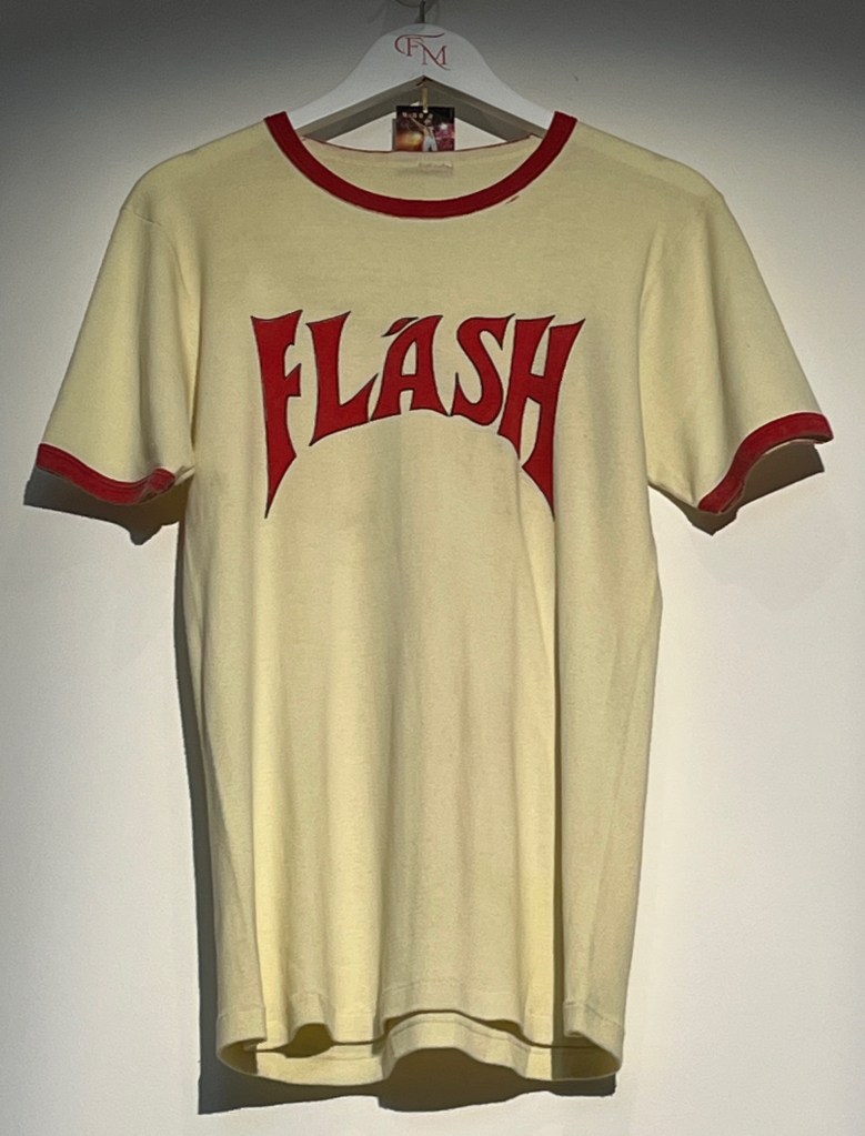 An ivory cotton T-shirt decorated on the front with large hand-stencilled lettering saying Flash, coloured in red and outlined in black.