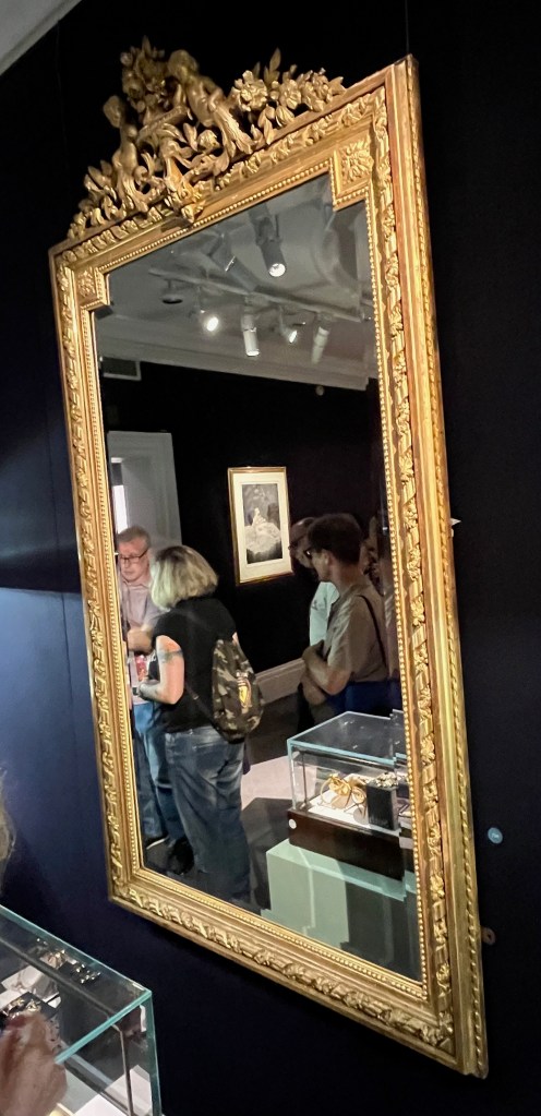 A large mirror with an ornate gold frame, the top section of which is carved with cherubs and flowers.