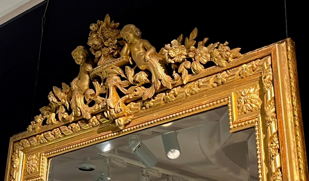 Close-up of the ornate gold carvings at the top of a mirror, with cherubs and flowers.
