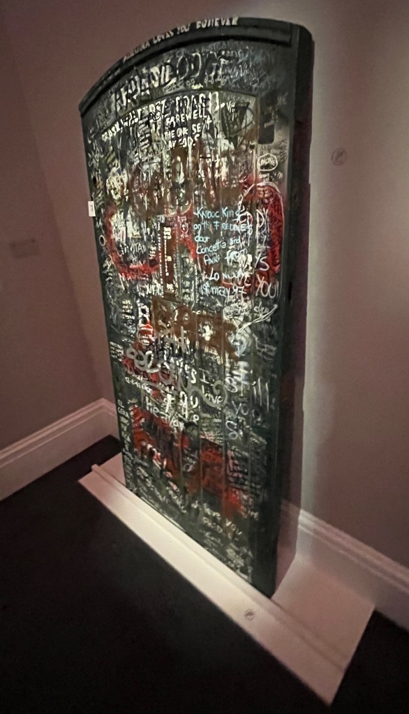 The large green door to Garden Lodge, viewed from an angle on the right to show its thickness. The door is covered in graffiti from fans in tribute to Freddie Mercury.