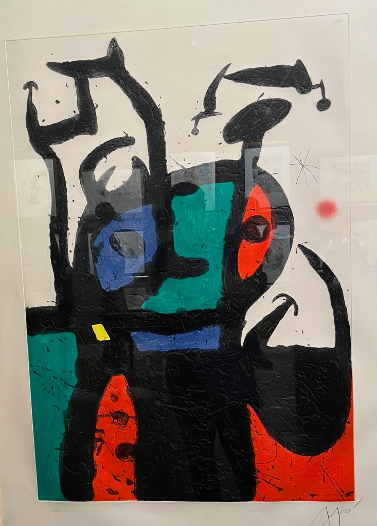 A print by Joan Miró called Le Matador, which is an abstract image made of bold black lines and a few colours. The central part appears to be an oval-shaped face, with an eye in a blue section on the left and another eye in a red sight on the right, with a larger empty green section between them. The entity then has a short blue neck and a black body beneath.