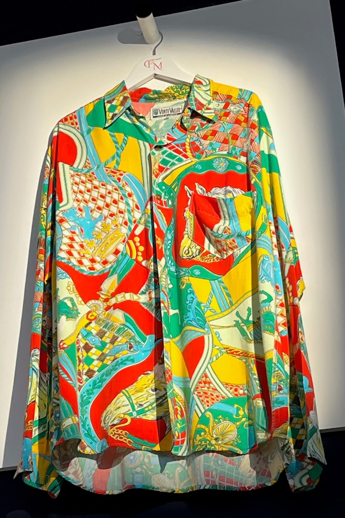 A brightly coloured long-sleeved cotton shirt printed with a design of crowns, horses and saddlery in red, green, yellow and turquoise, left breast pocket, fastening with imitation brown horn buttons.
