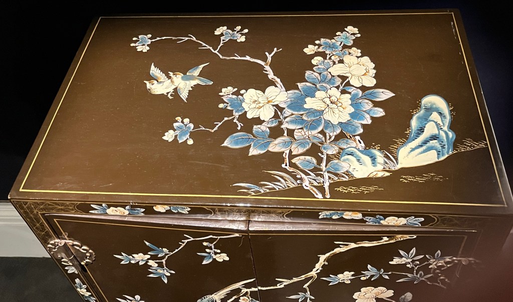 The top of a cabinet with painted decorations of flowering branches and birds.