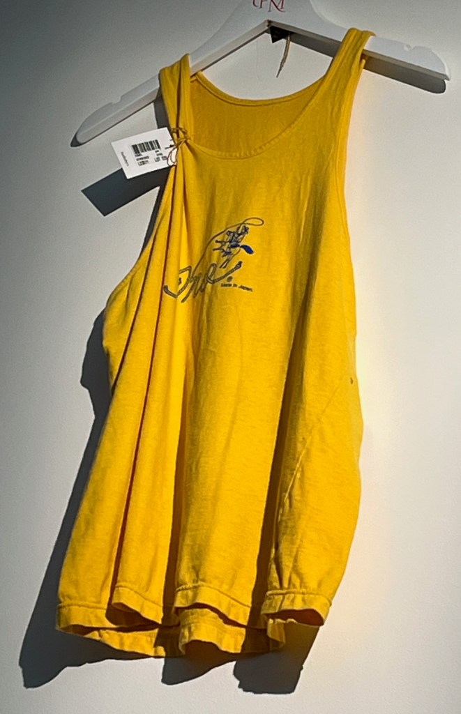 A yellow cotton vest, the front printed in blue with a small cowboy on a bucking horse, with an indecipherable word drawn with the cowboy’s lasso.