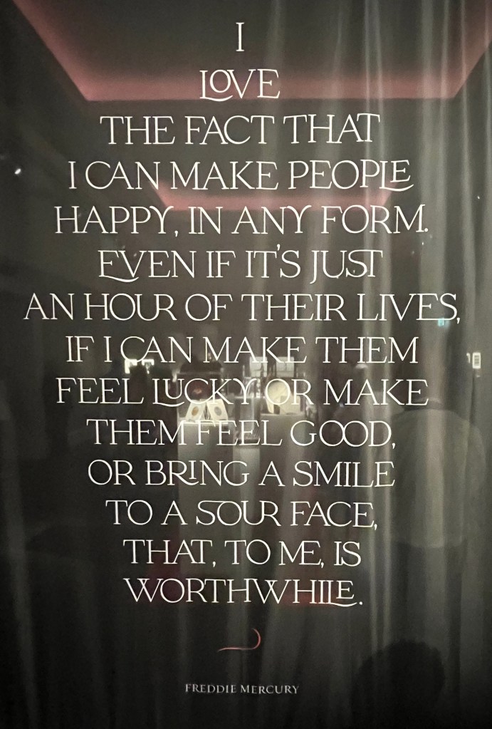 A quote by Freddie Mercury in large white text filling a large glass screen. It says I love the fact that I can make people happy, in any form. Even if it's just an hour of their lives, if I can make them feel lucky or make them feel good, or bring a smile to a sour face, that, to me, is worthwhile.