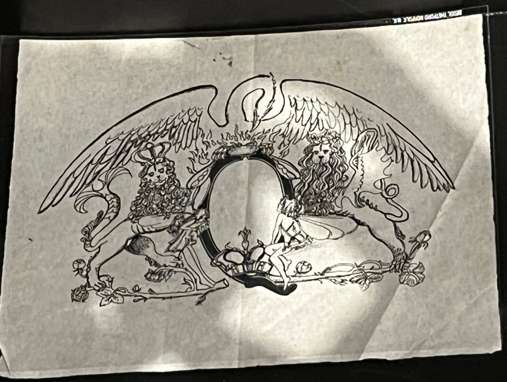 Freddie Mercury's ink drawing of the crest for the band Queen. . The crest resembles a heraldic coat of arms and incorporates the zodiac signs of the band members: fairies for Virgo (Mercury), lions for Leo (Deacon and Taylor) and a crab for Cancer (May). At its centre is a crown in a Q, and across the top is a phoenix with its wings spread across the width of the crest.