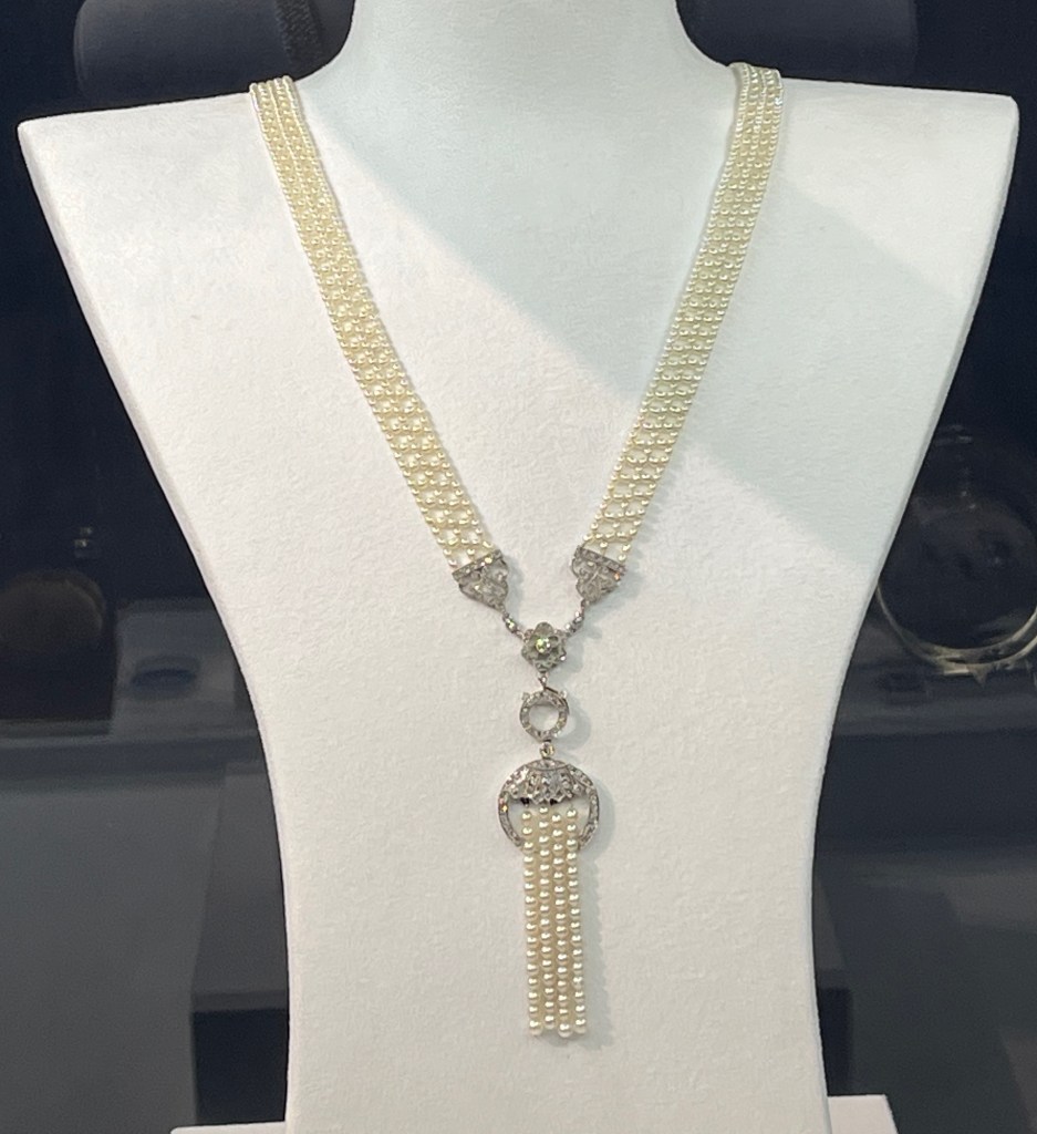 A long pearl and diamond necklace, with a section shaped a bit like a buckle and strap that hangs vertically at the bottom.
