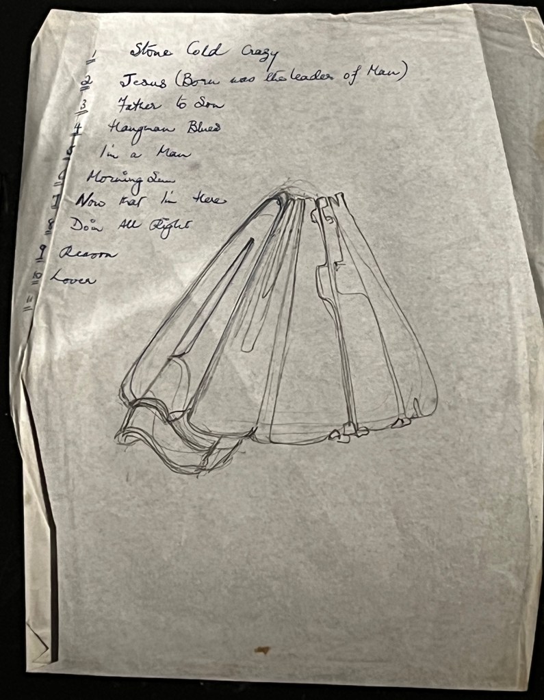 An early 1970s handwritten set list for Queen, including Stone Cold Crazy, Jesus (Born Was The Leader Of Man), Father To Son, Hangman Blues, I'm A Man, Morning Sun, Now That I'm Here, Doing All Right, Reason and Lover. The page also contains a sketch of the word Queen, in very large capital letters, which have been stretched upwards to meet at the top, making the word look like a skirt.